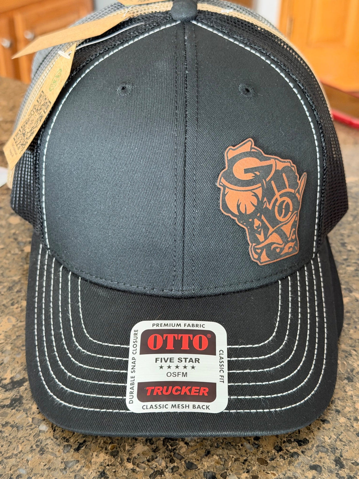 Black trucker hat with leather Wisconsin shape patch featuring state sports team logos