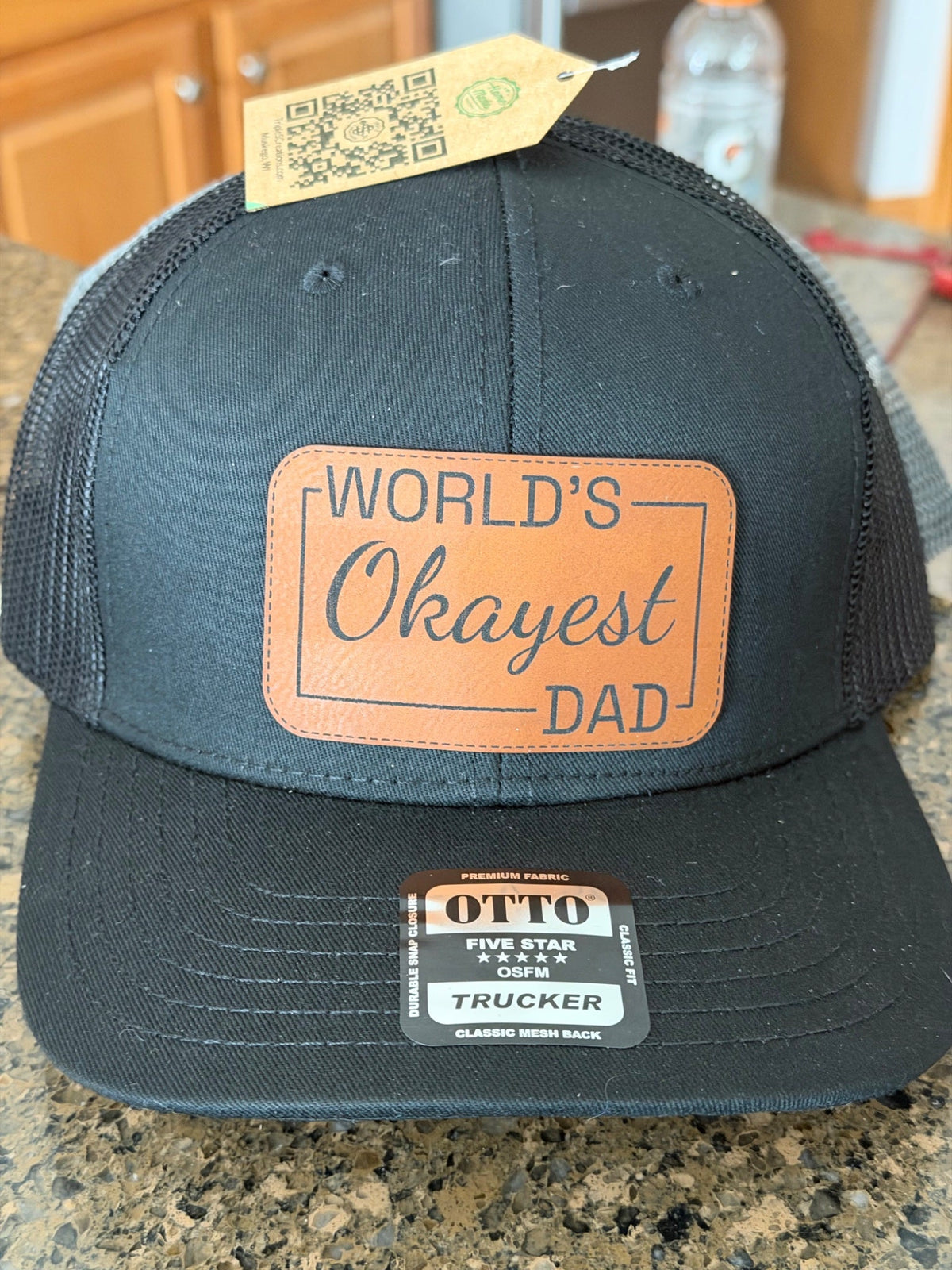 Black trucker hat with World's Okayest Dad leather patch